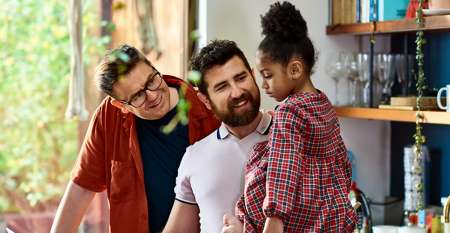 Two men in kitchen showing laptop screen to young girl