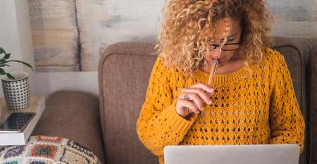 Woman on sofa holding pen using laptop