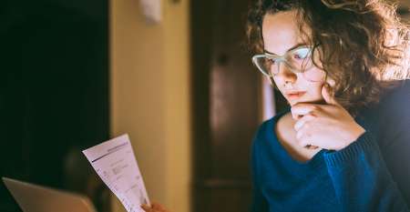 Young woman holding paper staring at laptop screen