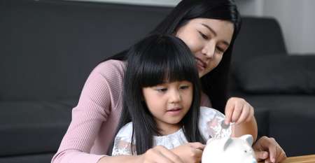 Young woman showing child how to use a piggybank