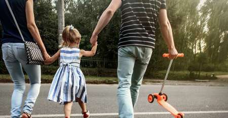Parents holding their little girl's hand crossing road to park