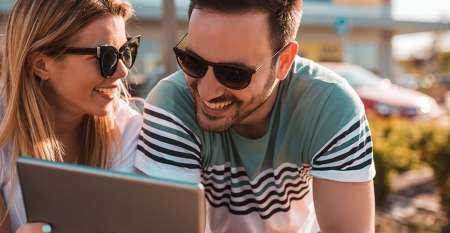 Young couple wearing sunglasses looking at tablet