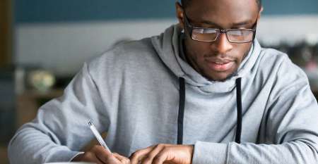 Young man at desk with laptop writing