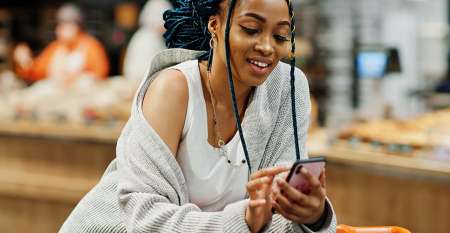 Young woman leaning over shopping trolley using mobile phone