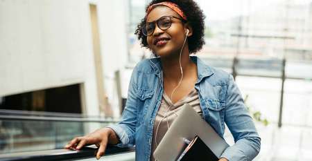 Young woman on escalator holding laptop listening to music