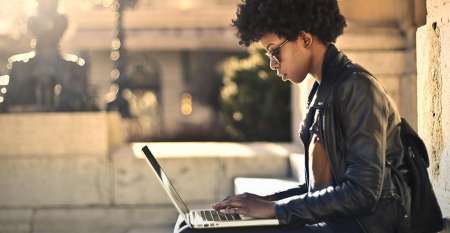 Young woman sitting on step outdoors using laptop